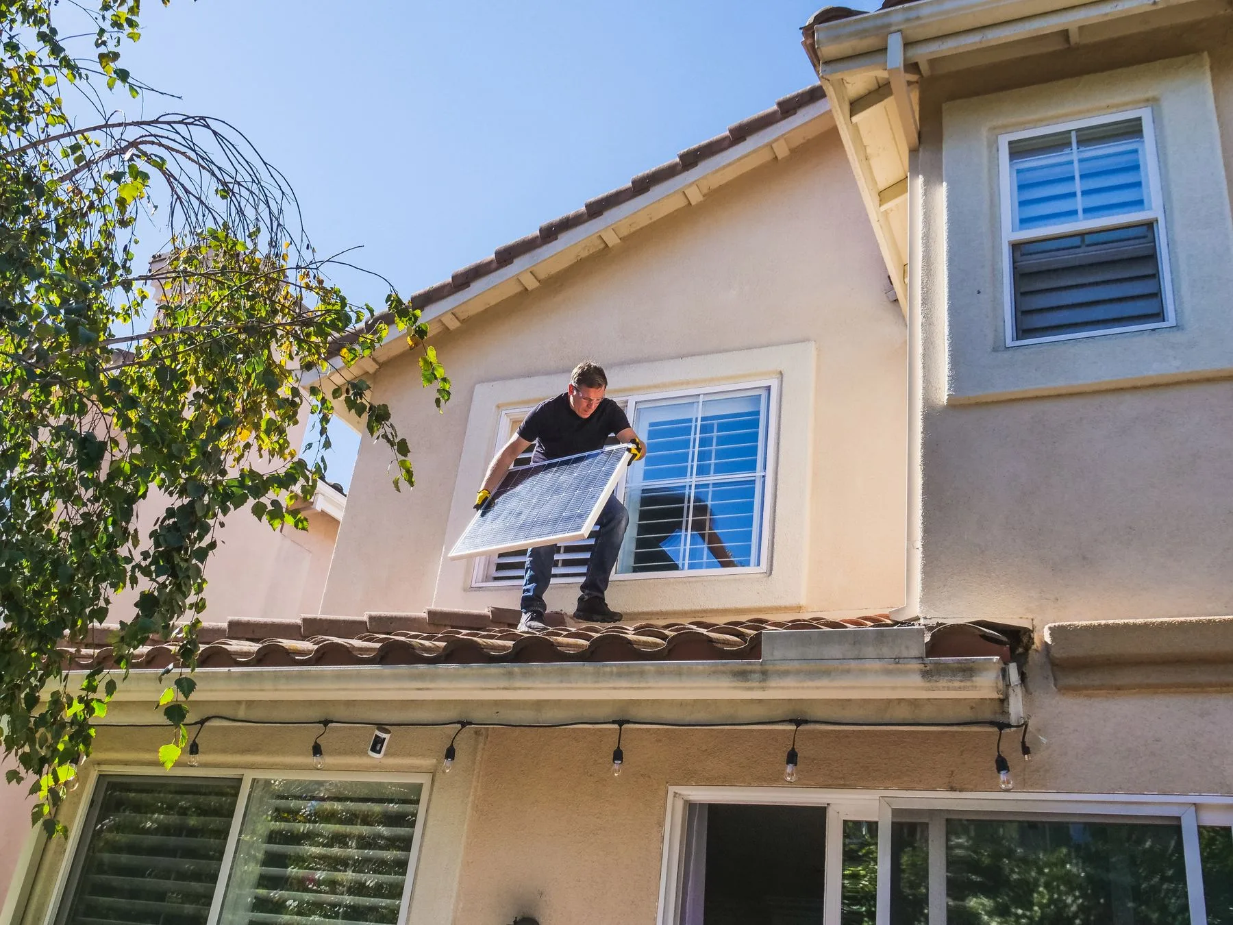 Solar technician carrying a panel on a residential roof.
